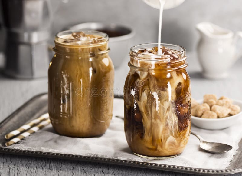 Mjölka att hällas in i ett exponeringsglas av med is kaffe arkivfoto