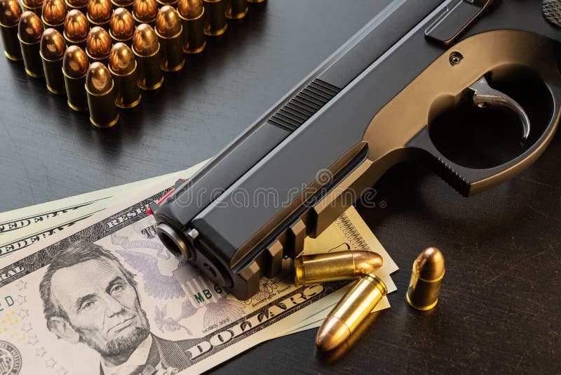 9 mm semi-automatic pistol and full metal jacket bullets on dollar banknotes laid out on black table. Conceptual mockup of gun control, crime, military-industrial complex or defense. 9 mm semi-automatic pistol and full metal jacket bullets on dollar banknotes laid out on black table. Conceptual mockup of gun control, crime, military-industrial complex or defense.