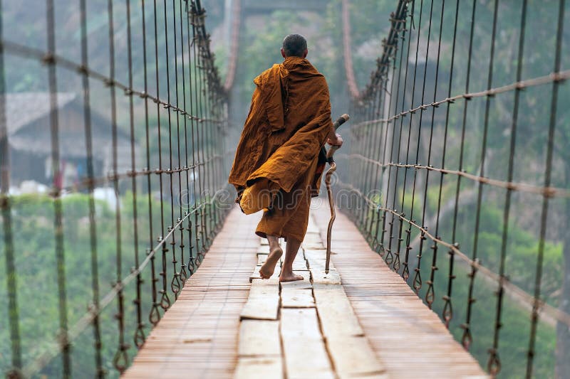 A monk with a walking stick Walk on a wooden suspension bridge in a small village in Mae Hong Son, Thailand. A monk with a walking stick Walk on a wooden suspension bridge in a small village in Mae Hong Son, Thailand