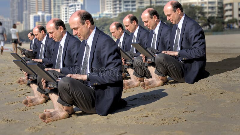 Una foto di imprenditori (clonato), seduto su di una spiaggia e di lavoro sul loro computer portatile.