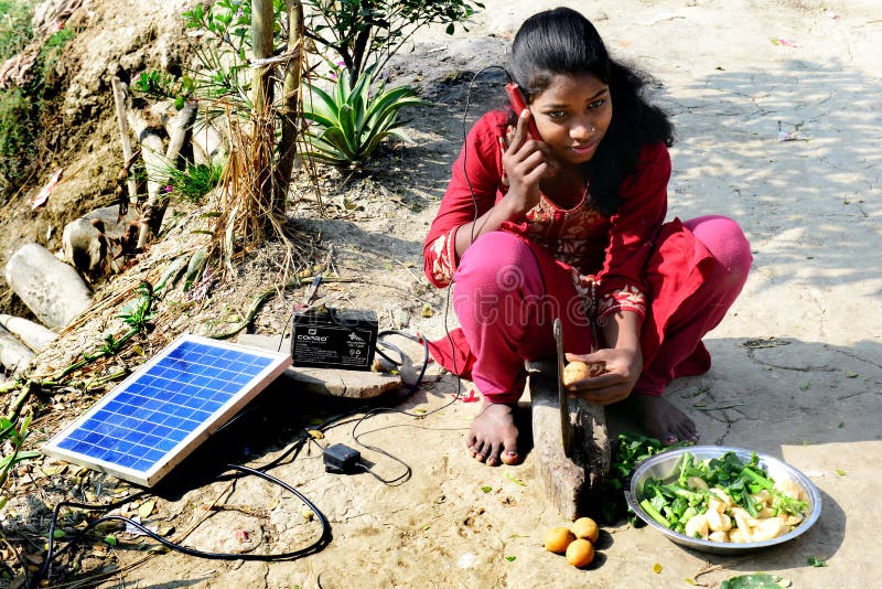 An adolescent girl talking at mobile phone beside a solar system in the rural village of West Bengal-India.