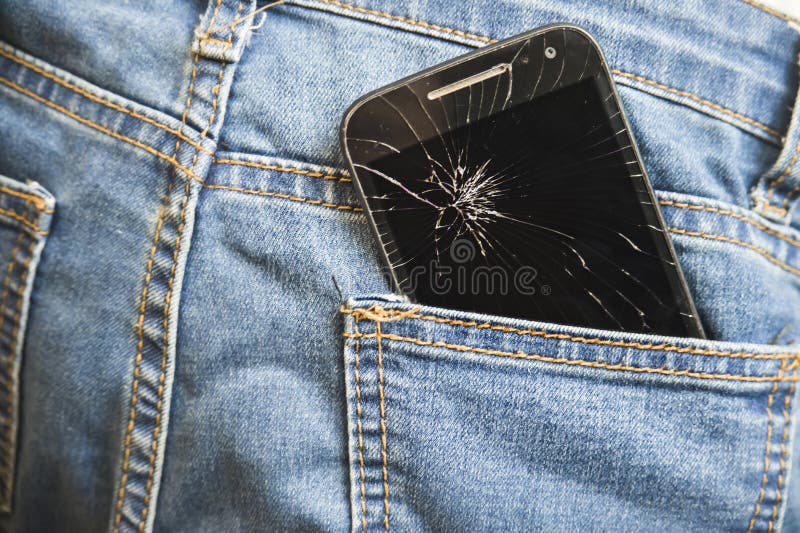 Mobile phone broken cracked touch screen in the back pocket of jeans denim trousers in accident and careless concept