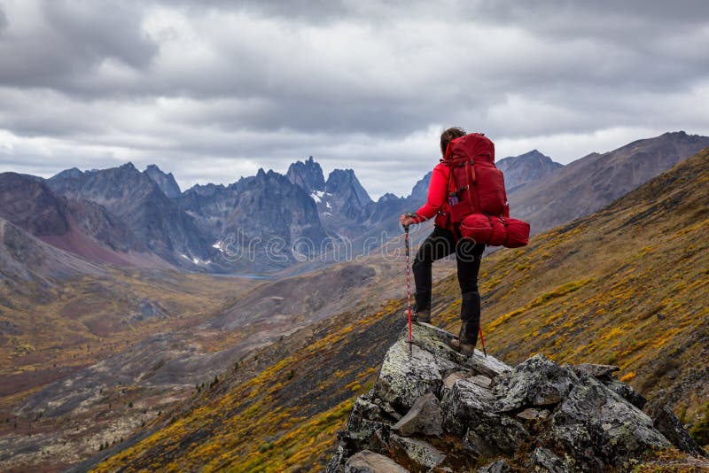 Woman Standing on Rocks looking at Scenic Mountain Peaks and Valley during Fall in Canadian Nature. Taken in Tombstone Territorial Park, Yukon, Canada. Woman Standing on Rocks looking at Scenic Mountain Peaks and Valley during Fall in Canadian Nature. Taken in Tombstone Territorial Park, Yukon, Canada.