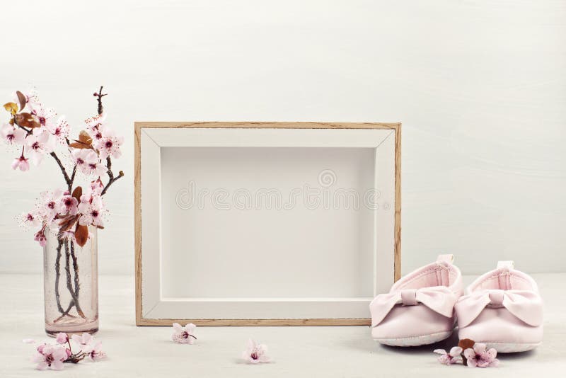 Mock up with empty picture frame, pink tender spring flowers and small baby girl shoes