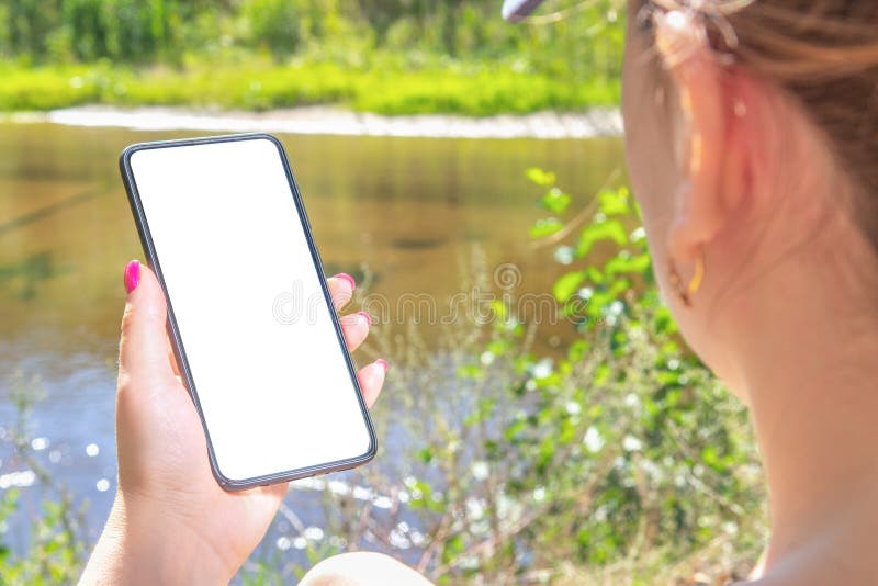Mockup image. Woman holds a phone with an empty screen, against the background of a pond and greenery royalty free stock photos