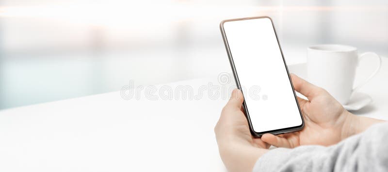 Mockup image of hand holding white mobile cellphone with blank screen with coffee cup on white table. wide banner mock up royalty free stock photography