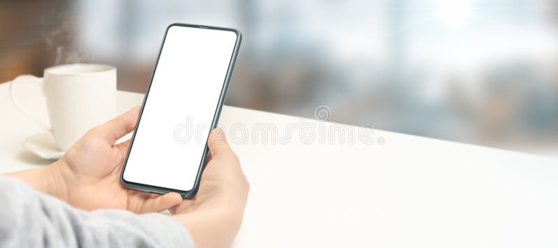 Mock up cellphone. Mockup image of hand holding white mobile cell phone with blank screen with coffee cup on white table royalty free stock photos