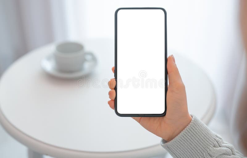 Mockup image woman holding black mobile phone with blank screen with coffee cup on table. woman`s hand holding cellphone with stock photography