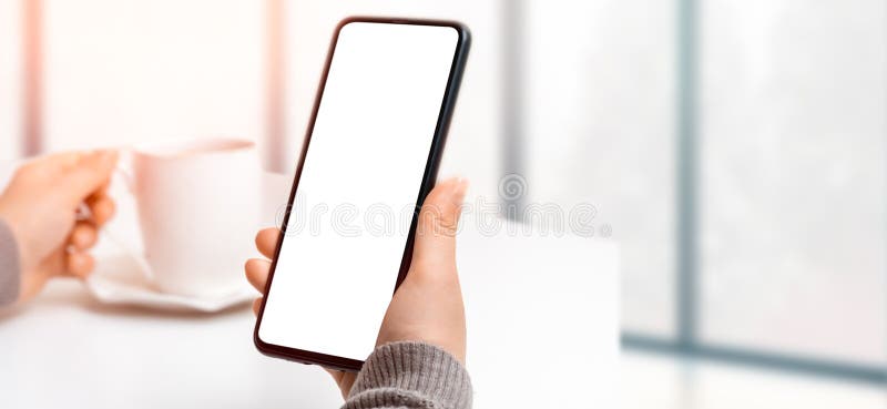Mockup image of woman`s hand holding black mobile phone with blank screen while drinking coffee. mockup cellphone. wide banner royalty free stock photo