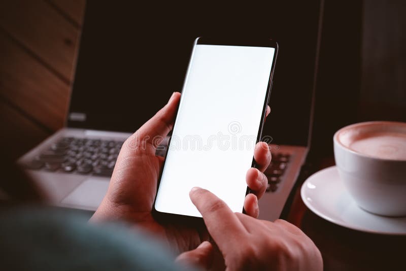 Mockup mobile phone image. Close up hands using modern smart phone Technology in coffee shop with blurred laptop and a cup of royalty free stock images