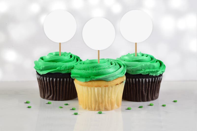 Three green frosted delicious cupcakes rest atop a white marble background surrounded by green sprinkles. Great St. Patrick`s Day or sports team cupcake mock up. Three green frosted delicious cupcakes rest atop a white marble background surrounded by green sprinkles. Great St. Patrick`s Day or sports team cupcake mock up