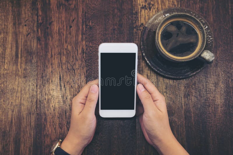 Mockup wizerunek biały telefon komórkowy z pustą czerni parawanową i gorącą filiżanką na rocznika drewna stołu tle obrazy stock