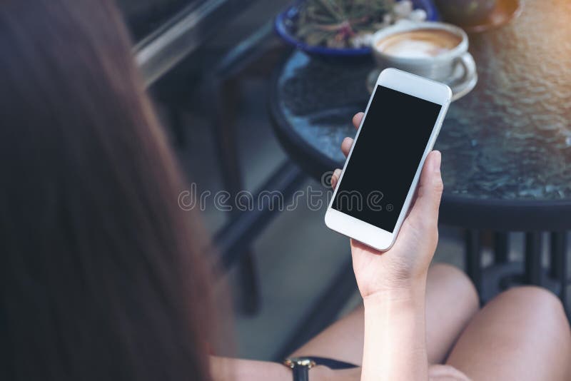 Mockup wizerunek kobiety ` s ręka trzyma białego telefon komórkowego z pustym czarnym desktop ekranem, filiżanką i obrazy stock