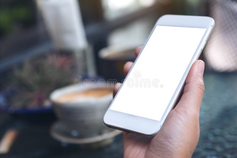 Mockup wizerunek kobiety ` s ręka trzyma białego telefon komórkowego z pustym desktop ekranem, filiżanką i fotografia stock