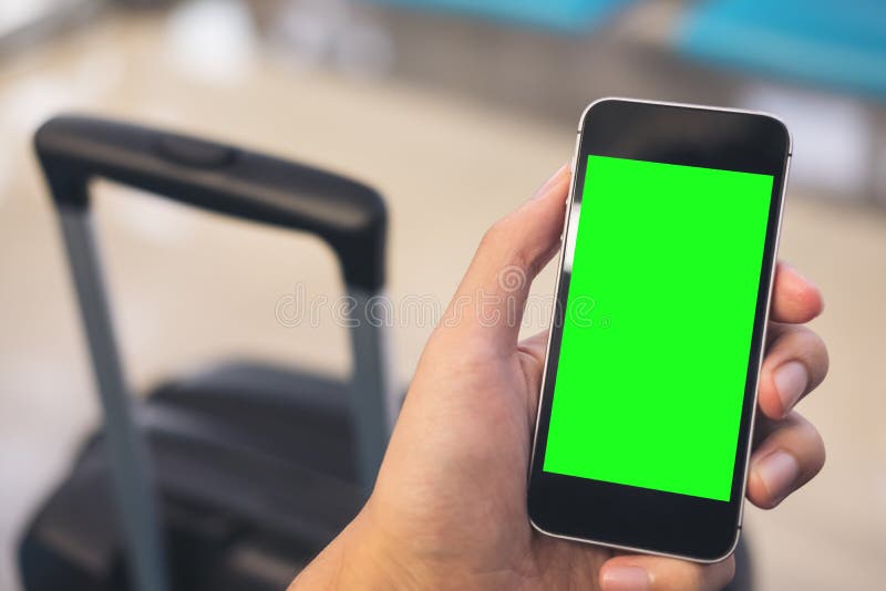 Mockup wizerunek mężczyzna ` s ręka trzyma czarnego telefon komórkowego z puste miejsce zieleni ekranem i używa. Mockup wizerunek mężczyzna ` s ręka trzyma czarnego telefon komórkowego z puste miejsce zieleni ekranem z czarnym bagażem i używa w lotnisku