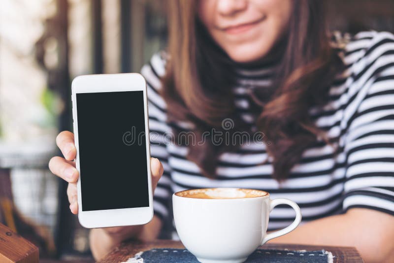 Mockup wizerunek piękna kobieta trzyma białego telefon komórkowego z pustym czerń ekranem z i pokazuje smiley twarzą o i filiżank obrazy stock