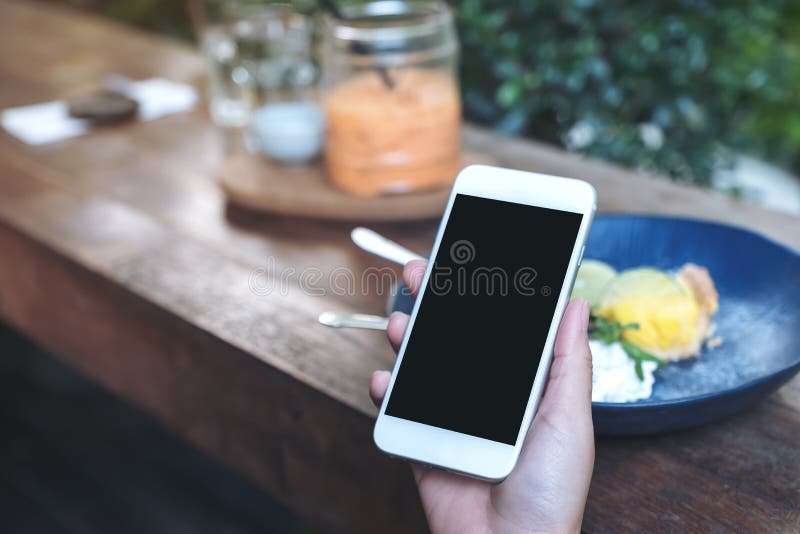 Mockup wizerunek ręki trzyma białego telefon komórkowego z pustym czerń ekranem podczas gdy jedzący żółtego cytryny curd tort na obraz royalty free