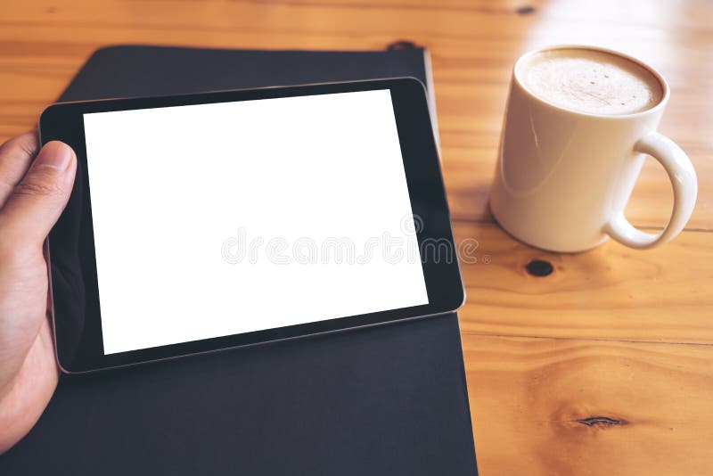 Mockup wizerunek trzyma czarnego pastylka komputer osobistego z pustym bielu ekranem na czarnej papieru i bielu filiżance na rocz obraz royalty free