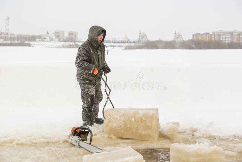 A worker pulls an ice block out of the hole with steel tongs. A worker pulls an ice block out of the hole with steel tongs