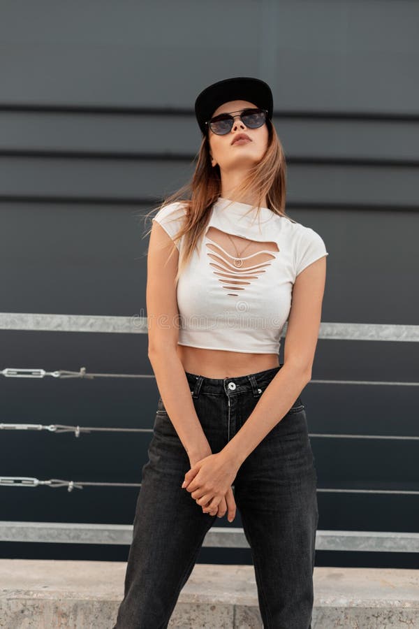 Hipster Mujer Moderna Y Elegante Con Una Gorra Negra De Moda En Camiseta  Sexy Rota En Jeans En Gafas De Sol De Moda Relaja Cerca D Imagen de archivo  - Imagen de