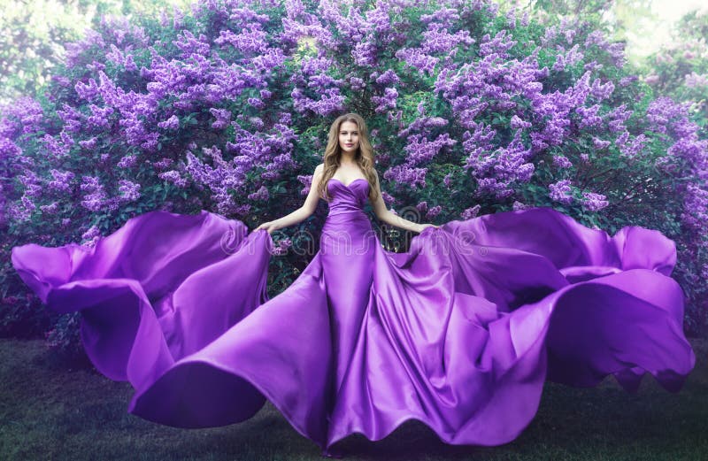 Mode-Modell in der jungen Frau der lila Blumen im schönen langen Kleid, das auf Schönheitsporträt des Windes im Freien in blühende
