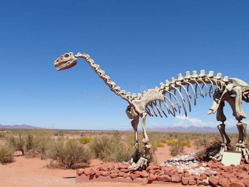 The statue, a model dinosaur standing on a red dry sand between the rocks. Artificial dinosaur. Jurassic Park. Models of dinosaurs in the museum, the National Park talampaya outdoors in Argentina. The statue, a model dinosaur standing on a red dry sand between the rocks. Artificial dinosaur. Jurassic Park. Models of dinosaurs in the museum, the National Park talampaya outdoors in Argentina.