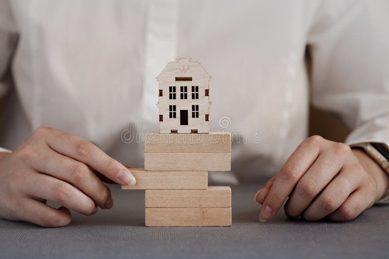 Model of a House on a Tower of Blocks, a Hand Pulls Out a Brick, Risks