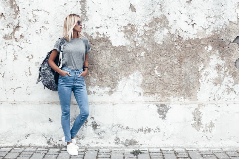 Young woman in stylish tight jeans, wearing crop top with handbag walking  outdoors in summer season, rear view. Woman wearing blue skinny jeans and crop  top shirts walking on city street. Stock