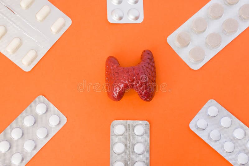 Model of thyroid gland surrounded by six blister packs with white pills inside in corners of image on orange background. Photo co stock images