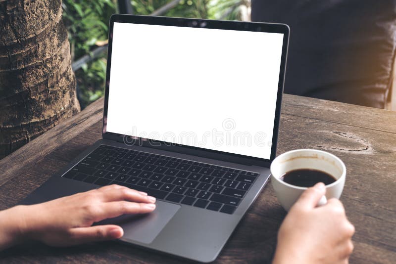 Modelbeeld van een vrouw die laptop met het lege witte scherm met behulp van terwijl het drinken van koffie op houten lijst stock foto's Modelbeeld van een vrouw die laptop met het lege witte scherm met behulp van terwijl het drinken van koffie op houten lijst stock foto's