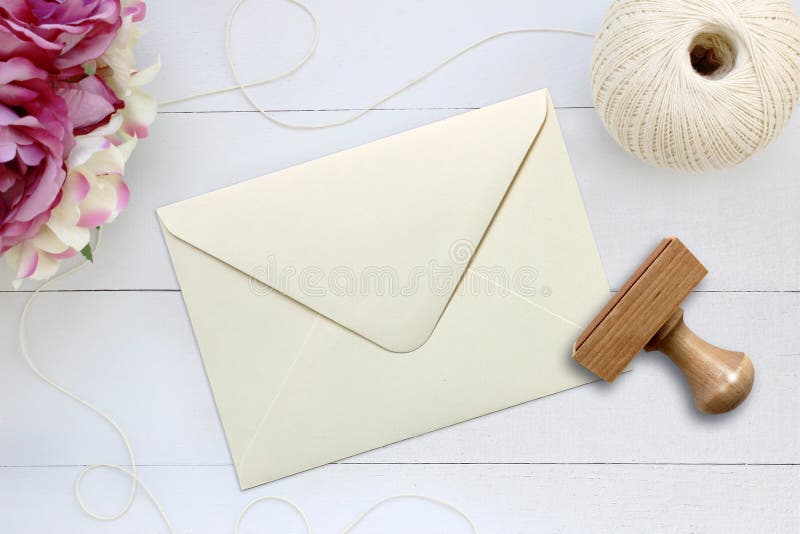 Mockup of ivory envelope with a rubber stamp next to it. Modern trend template for advertising. Delicate wooden background with flowers. Mockup of ivory envelope with a rubber stamp next to it. Modern trend template for advertising. Delicate wooden background with flowers.