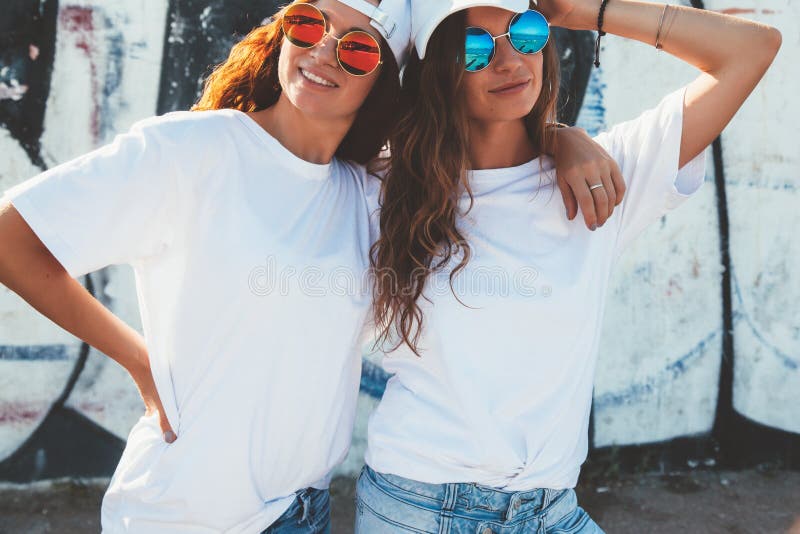 Two models wearing plain white t-shirts and hipster sunglasses posing against street wall. Teen urban clothing style, same look. Mockup for tshirt print store. Two models wearing plain white t-shirts and hipster sunglasses posing against street wall. Teen urban clothing style, same look. Mockup for tshirt print store.