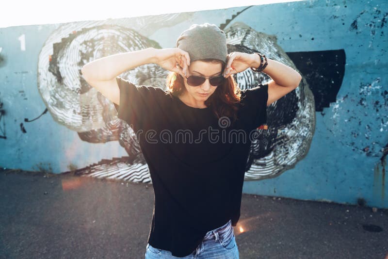 Model wearing plain black t-shirt and hipster sunglasses posing against street wall, teen urban clothing style, mockup for tshirt print store. Model wearing plain black t-shirt and hipster sunglasses posing against street wall, teen urban clothing style, mockup for tshirt print store