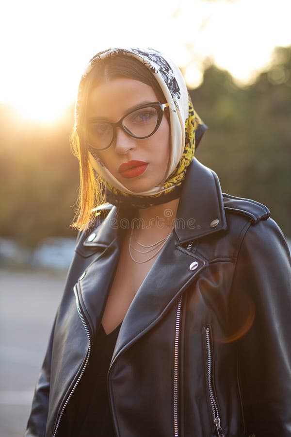 Modello castana alla moda con trucco luminoso che porta sciarpa capa che posa su una via con abbagliamento del sole fotografie stock Modello castana alla moda con trucco luminoso che porta sciarpa capa che posa su una via con abbagliamento del sole fotografie stock