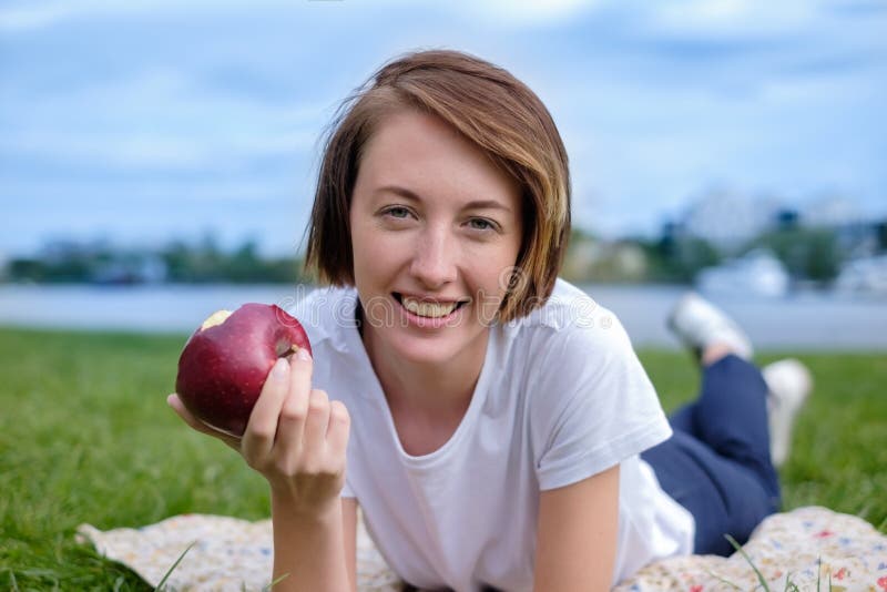Modello caucasico molto bello che mangia mela rossa nel parco All'aperto ritratto della ragazza graziosa fotografia stock Modello caucasico molto bello che mangia mela rossa nel parco All'aperto ritratto della ragazza graziosa fotografia stock