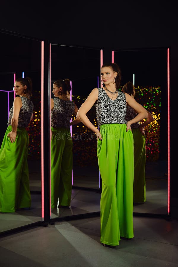 Modello che presenta pantaloni verdi vibranti e top elegante in un ambiente moderno riflettente fotografia stock