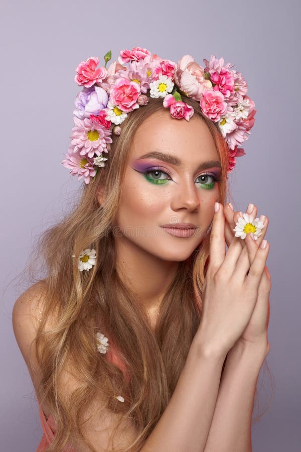 Modello che presenta un trucco vivace con puri e verdi ornati da una corona floreale colorata. Lei pone con grazia le mani fotografia stock