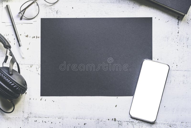 Modello dello strato di carta nero in bianco, smartphone, vetri dell'occhio, cuffie sullo scrittorio di legno autentico bianco na immagine stock libera da diritti Modello dello strato di carta nero in bianco, smartphone, vetri dell'occhio, cuffie sullo scrittorio di legno autentico bianco na immagine stock libera da diritti