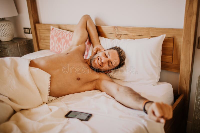 Modello gay maschio sexy senza camicia che si trova da solo sul suo letto nella sua camera da letto Tipo spensierato che gode di immagini stock