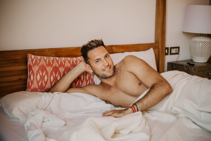 Modello maschio sexy senza camicia che si trova da solo sul suo letto nella sua camera da letto, esaminante la macchina fotografi immagini stock libere da diritti