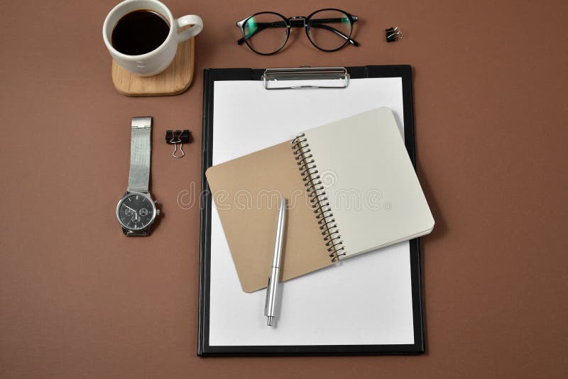 Modellworkspace med det tomma gembrädet, kontorstillförsel, klockan, pennan, kaffekoppen, notepaden och glasögon på brun bakgrund fotografering för bildbyråer Modellworkspace med det tomma gembrädet, kontorstillförsel, klockan, pennan, kaffekoppen, notepaden och glasögon på brun bakgrund fotografering för bildbyråer