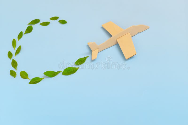 Modelo de avión de madera que emite hojas verdes frescas sobre fondo azul. viajes sostenibles energía limpia y verde y biocombusti