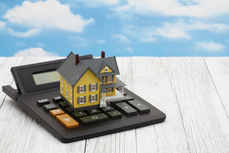 Model house on a calculator on weathered whitewash wood with clear blue sky. Model house on a calculator on weathered whitewash wood with clear blue sky