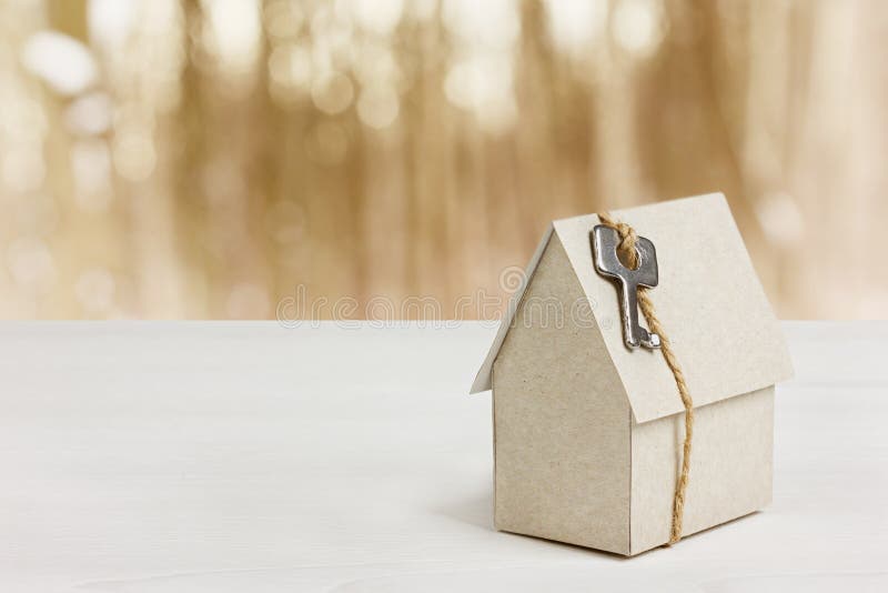 Model of cardboard house with key against bokeh background. house building, loan, real estate or buying a new home concept. Model of cardboard house with key against bokeh background. house building, loan, real estate or buying a new home concept.