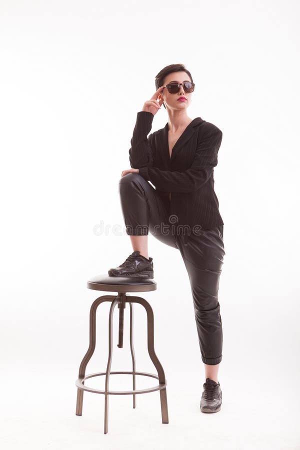 Modelo de moda joven en la ropa de moda y casual que presenta en estudio usando una silla sobre el fondo blanco fotografía de archivo libre de regalías Modelo de moda joven en la ropa de moda y casual que presenta en estudio usando una silla sobre el fondo blanco fotografía de archivo libre de regalías