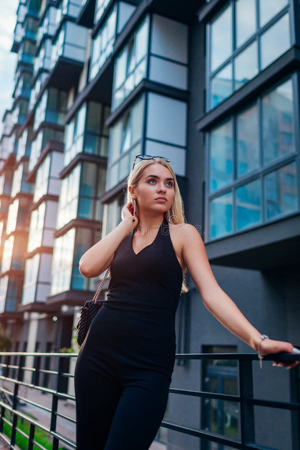 Modelo de moda de la belleza que lleva la ropa y los accesorios negros formales al aire libre Chica joven rubia que camina en la fotografía de archivo libre de regalías Modelo de moda de la belleza que lleva la ropa y los accesorios negros formales al aire libre Chica joven rubia que camina en la fotografía de archivo libre de regalías