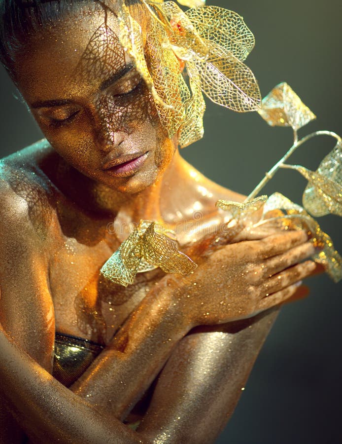 Modelo de oro de alta moda mujer con brillantes dorados brillantes en el retrato de flor de fantasía de la piel de hermosa muchach