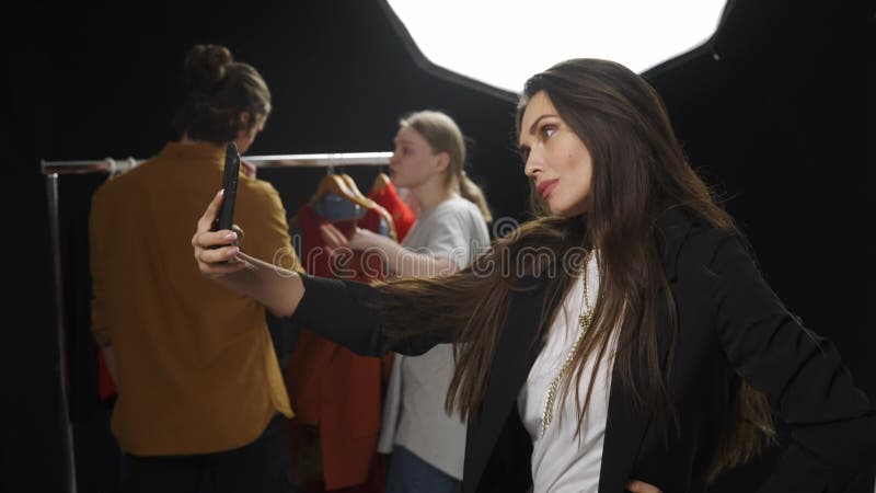 Modelo e equipe de produção no estúdio. fotógrafo e assistente de estilista de moda escolhendo modelo de roupa tirando selfie