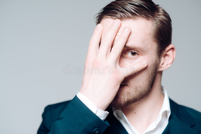 Modelo louro isolado no fundo cinzento Indiv?duo farpado com os olhos c?r de avel? que cobrem sua cara com a palma imagens de stock royalty free Modelo louro isolado no fundo cinzento Indiv?duo farpado com os olhos c?r de avel? que cobrem sua cara com a palma imagens de stock royalty free