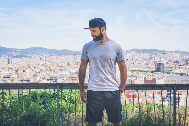 Modelo masculino hermoso del inconformista con la barba que lleva la camiseta en blanco gris y un casquillo negro del snapback co imagen de archivo Modelo masculino hermoso del inconformista con la barba que lleva la camiseta en blanco gris y un casquillo negro del snapback co imagen de archivo